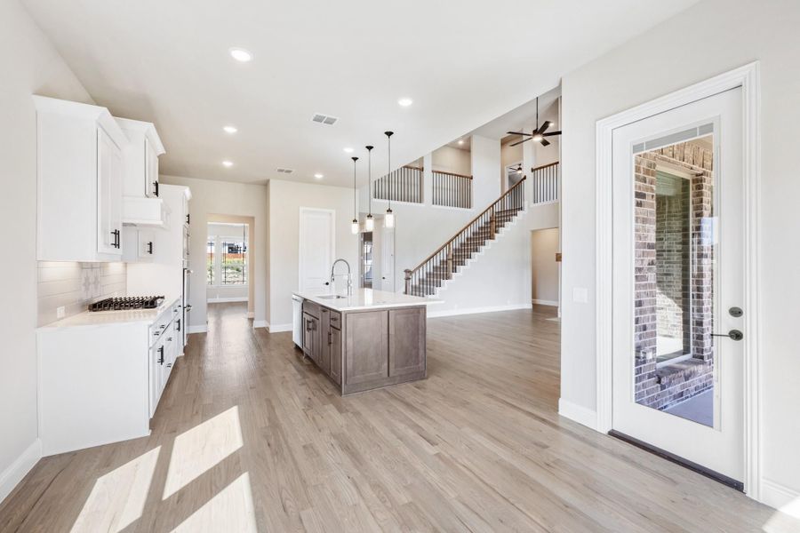 Open kitchen with white cabinets, dark wood island, and hardwood floors leading to a staircase