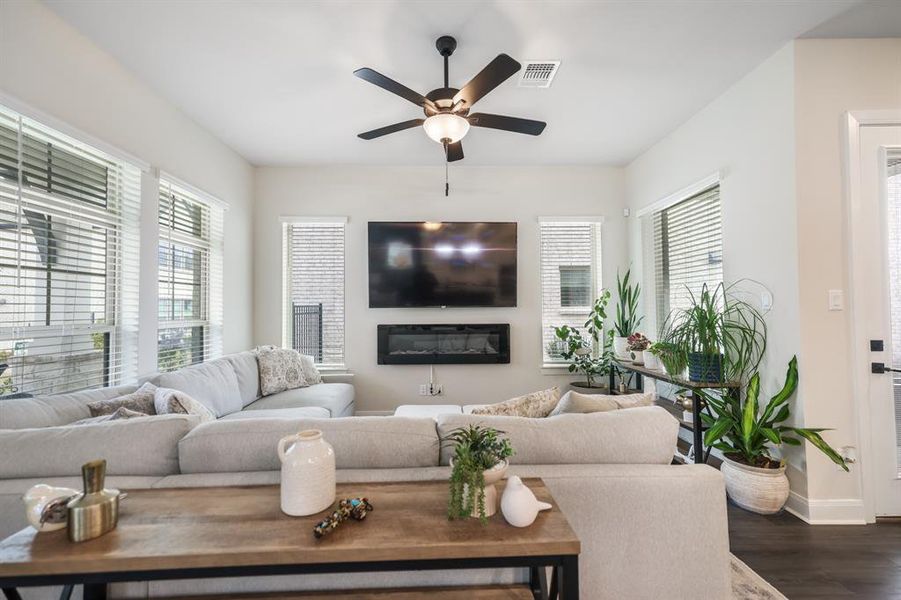 Living area with ceiling fan, dark wood-type flooring, and a glass covered fireplace