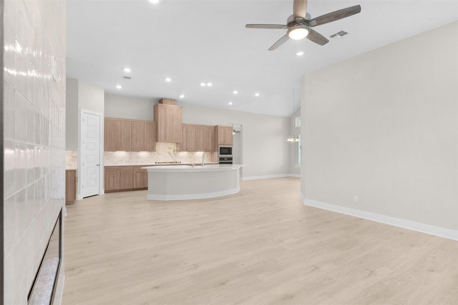Kitchen featuring open floor plan, decorative backsplash, a center island with sink, light brown cabinets, and light countertops Kitchen featuring open floor plan, decorative backsplash, a center island with sink, light brown cabinets, and light countertops
