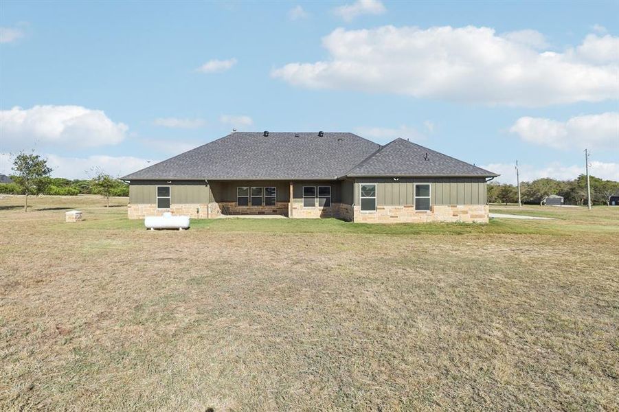 Back of property featuring stone siding, board and batten siding, a lawn, and a shingled roof Back of property featuring stone siding, board and batten siding, a lawn, and a shingled roof