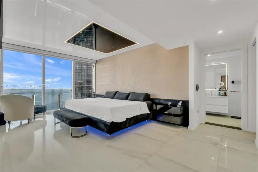 Floor-to-ceiling glass windows, recessed ceiling feature with integrated lighting, custom wall detailing, stone-finish flooring, and built-in vanity Floor-to-ceiling glass windows, recessed ceiling feature with integrated lighting, custom wall detailing, stone-finish flooring, and built-in vanity