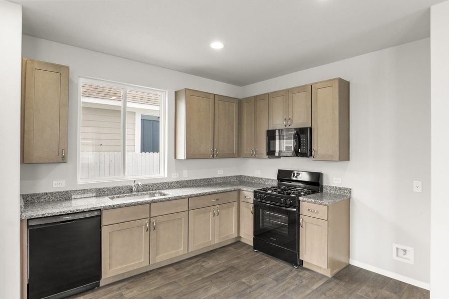 Image of a kitchen with light brown cabinets and black appliances with a window above the sink Image of a kitchen with light brown cabinets and black appliances with a window above the sink