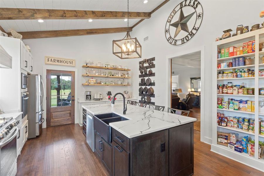 Expansive farmhouse-style kitchen featuring soaring beamed ceilings, a statement island with quartz countertops, and a gas range with convection oven—designed for both everyday cooking and effortless entertaining.