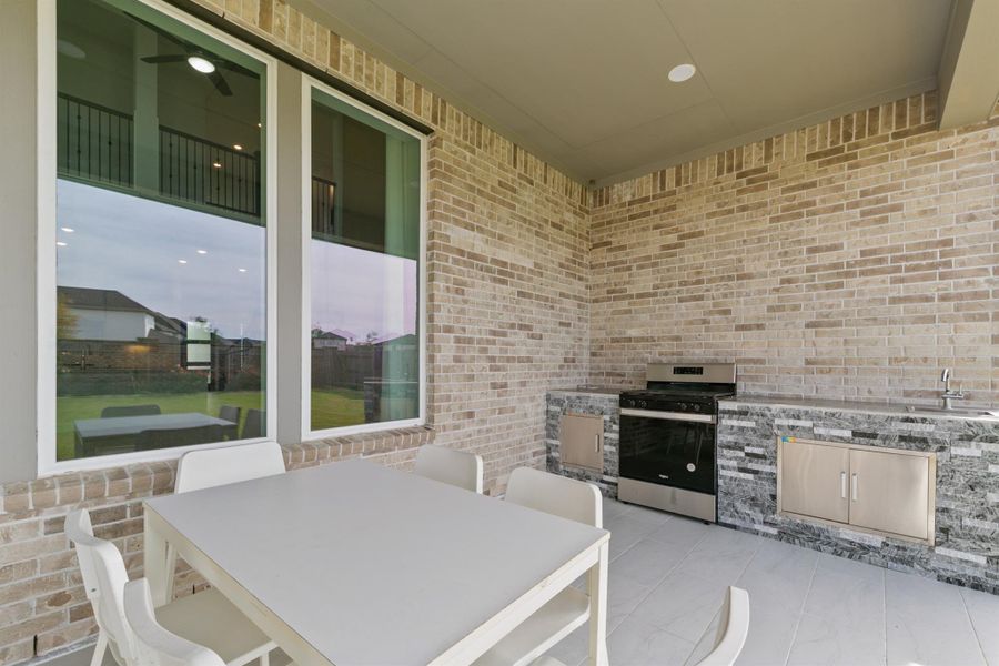 Covered outdoor patio featuring a built-in grill and countertop space, perfect for entertaining and weekend cookouts. Surrounded by a beautiful stone finish and large windows, this space offers a seamless indoor-outdoor living experience.