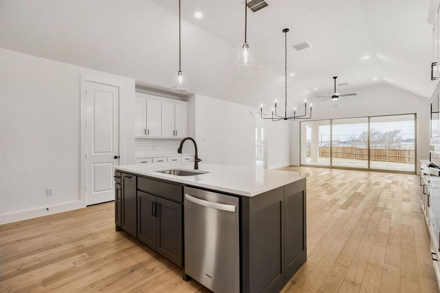 Dual tone kitchen featuring two tone cabinets, stainless steel appliances, lofted ceiling, an island with sink, and light wood finished floors