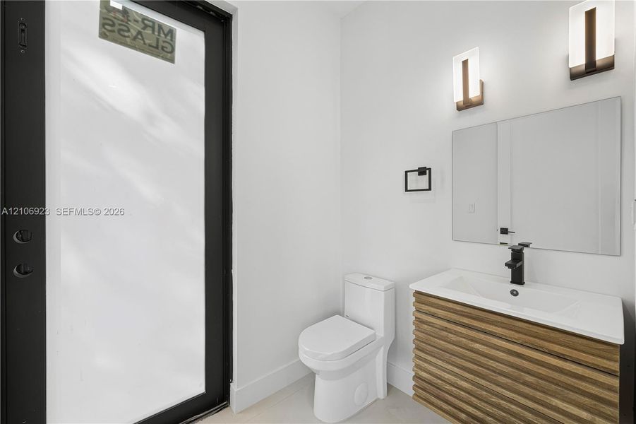 Floating vanity featuring wood-finish reeded detailing, white integrated countertop, matte black faucet, wall-mounted rectangular mirror, and dual vertical sconces Floating vanity featuring wood-finish reeded detailing, white integrated countertop, matte black faucet, wall-mounted rectangular mirror, and dual vertical sconces