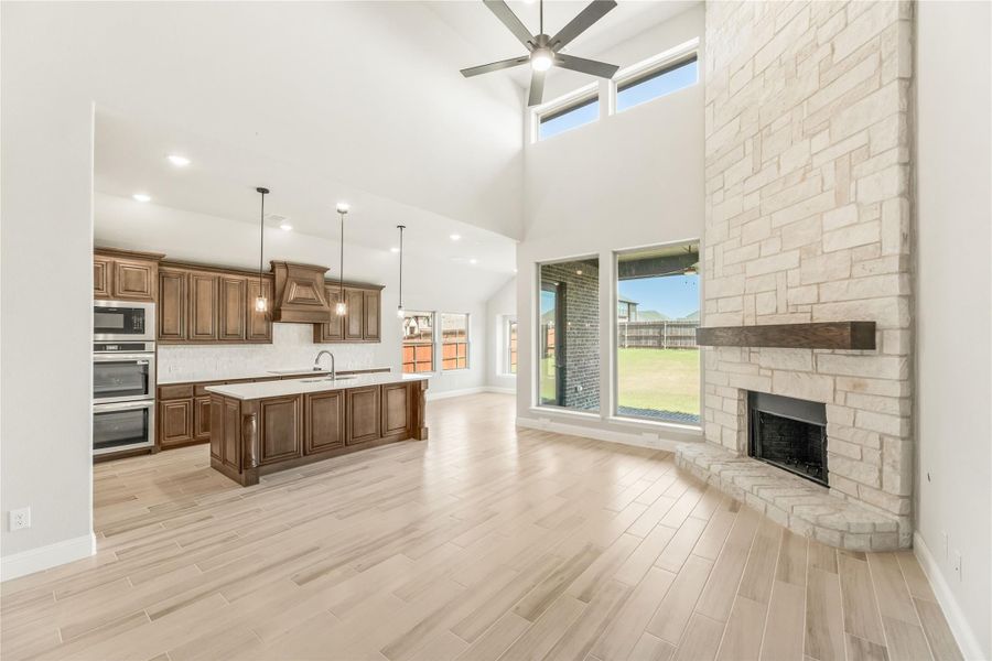 Open living area with stone fireplace, high ceilings, and kitchen with dark wood cabinets and large island Open living area with stone fireplace, high ceilings, and kitchen with dark wood cabinets and large island