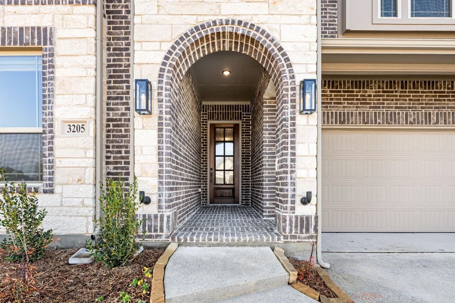 Home entrance with arched brick doorway, wall sconces, and glass front door next to a garage Home entrance with arched brick doorway, wall sconces, and glass front door next to a garage