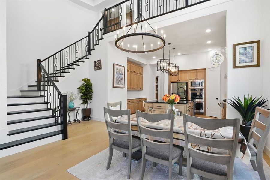 Dining area featuring light wood finished floors, stairway, recessed lighting, a towering ceiling, and a chandelier Dining area featuring light wood finished floors, stairway, recessed lighting, a towering ceiling, and a chandelier