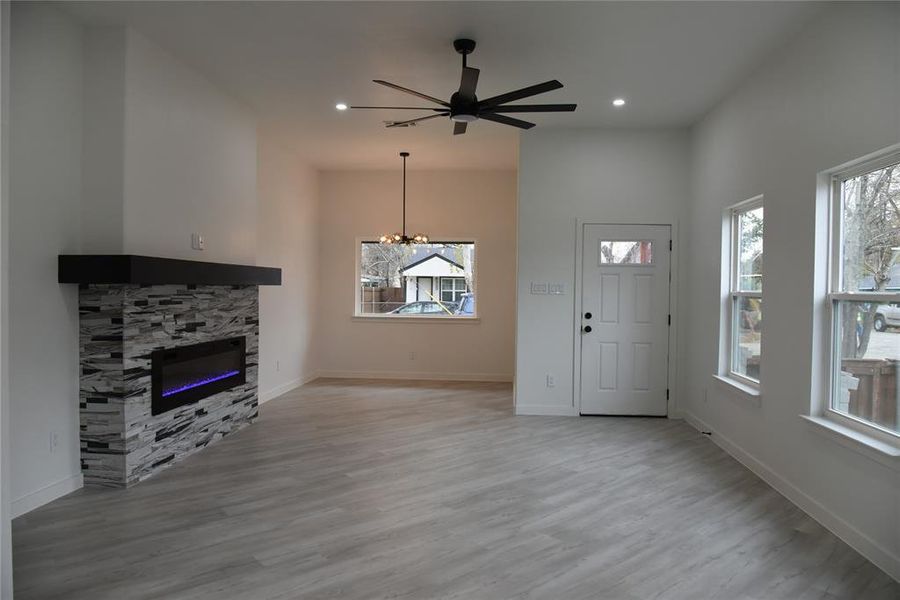 Unfurnished living room with a fireplace, light wood-type flooring, and ceiling fan with notable chandelier