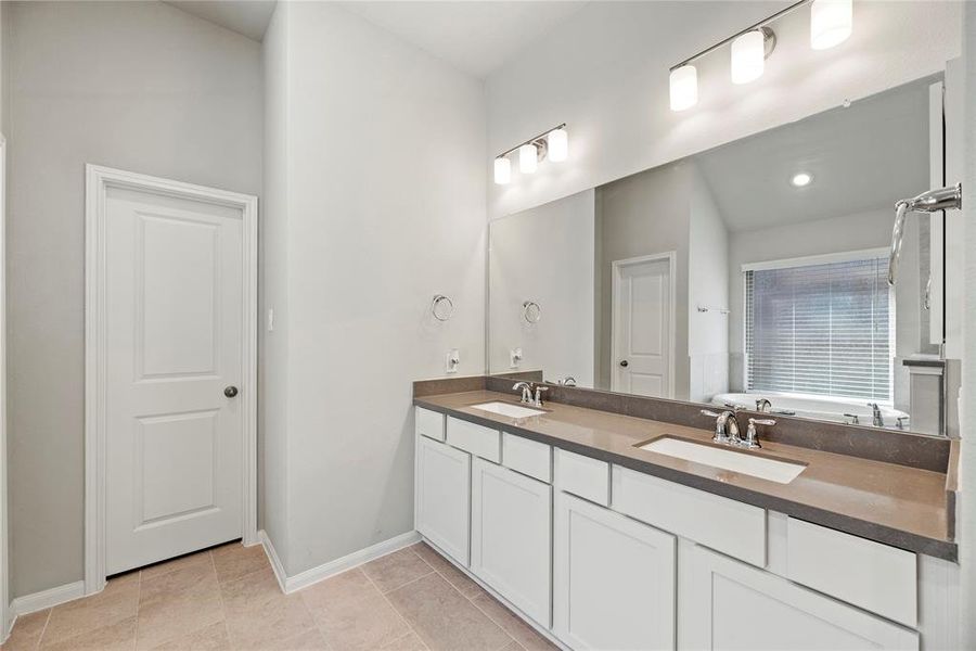 Primary bathroom with dual vanity sinks and a walk-in closet