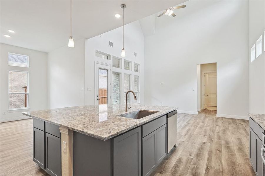 Kitchen featuring dishwasher, a high ceiling, a center island with sink, sink, and light hardwood / wood-style floors