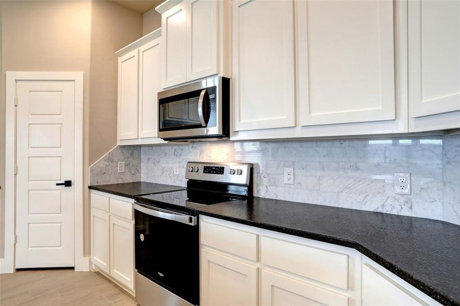 Kitchen with tasteful backsplash, light hardwood / wood-style flooring, stainless steel appliances, and white cabinets