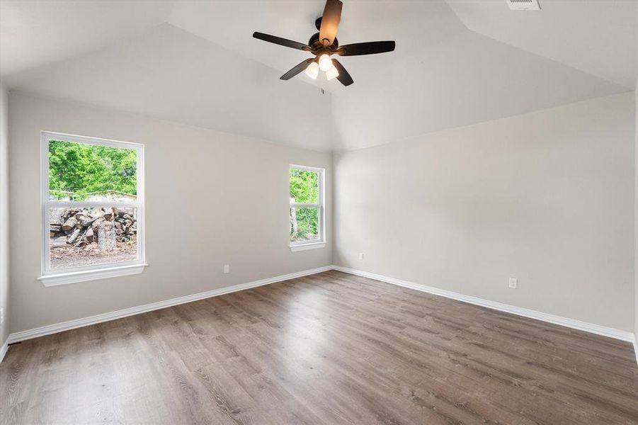 Spacious room featuring vaulted ceilings, wood-finish flooring, white baseboards, and two windows