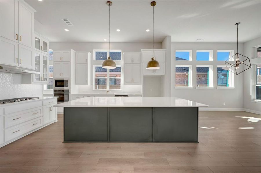 Dual tone kitchen featuring dual tone cabinetry, a spacious island, light wood-style flooring, stainless steel appliances, and glass insert cabinets