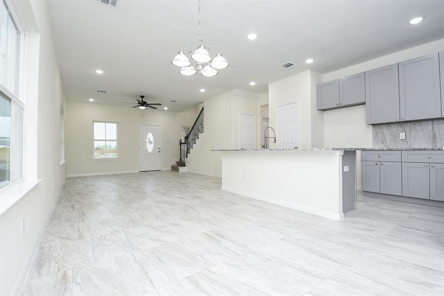 An Modern kitchen with gray cabinets and a living area with tiled flooring, large windows, and a staircase in the background.