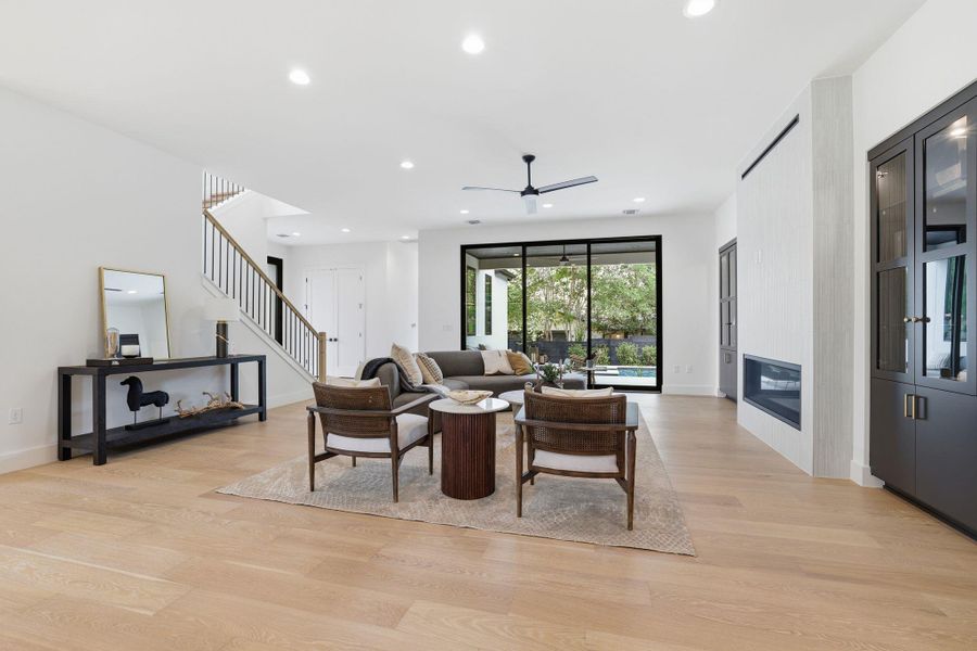 Open-concept living space featuring wood-finish flooring, a contemporary linear fireplace, and integrated dark wood cabinetry with glass fronts