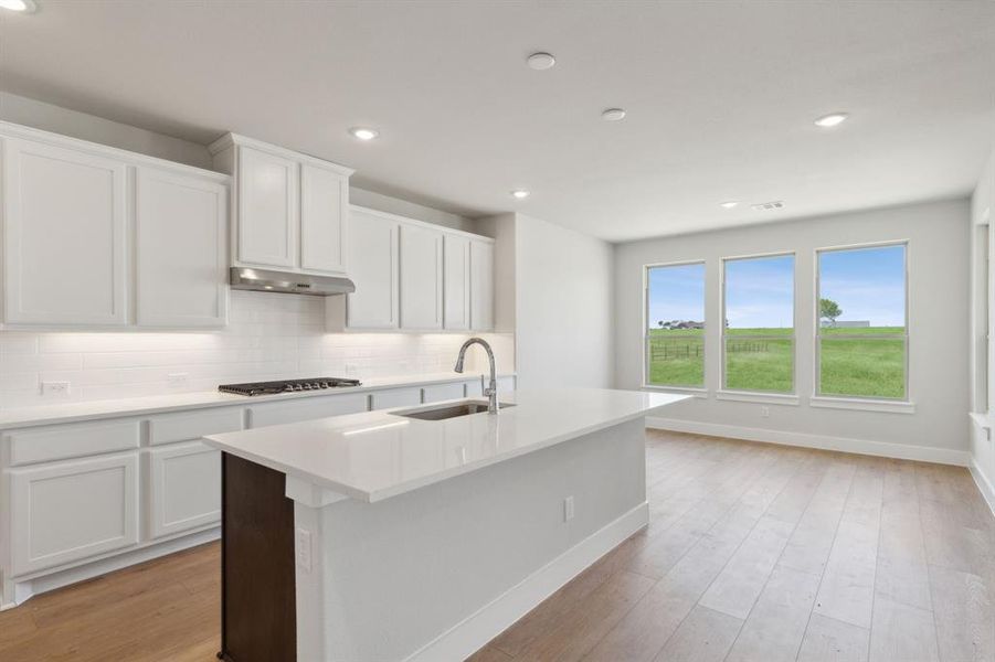 Kitchen featuring white cabinets, sink, light hardwood / wood-style flooring, backsplash, and a kitchen island with sink