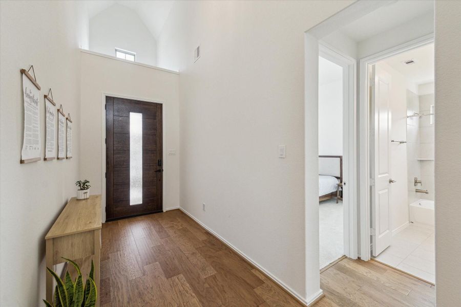 The reverse view from the foyer showcases the striking front door with its rectangular perpendicular window, complemented by a statement chandelier and a decorative niche above, adding architectural interest and natural light.