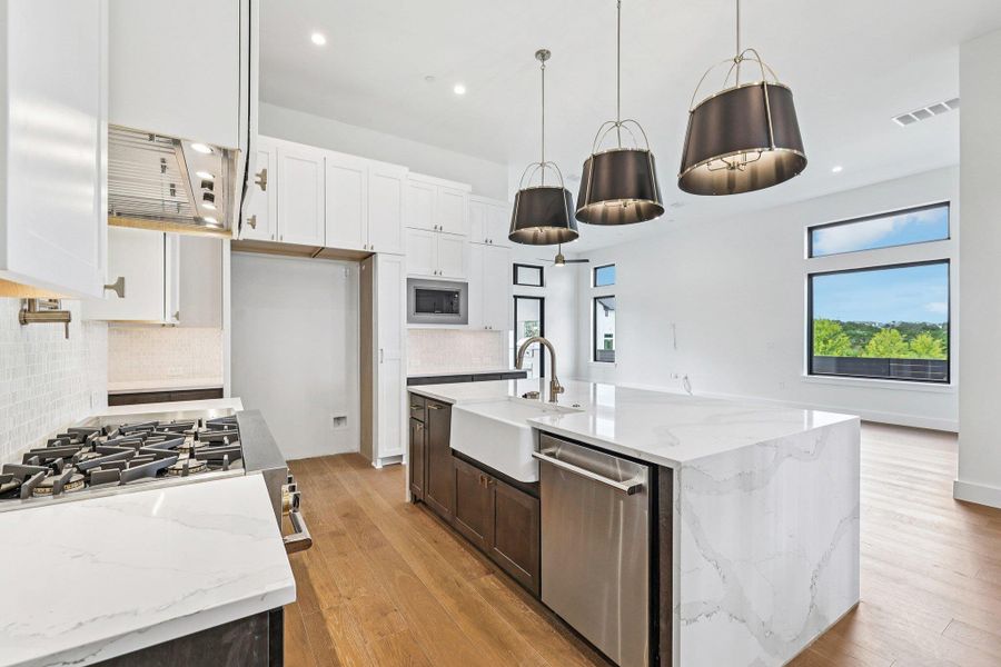 Kitchen featuring light stone counters, decorative backsplash, white cabinetry, a kitchen island with sink, and light wood-style flooring