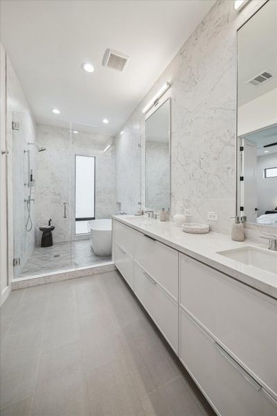 Long, gallery-style primary bath showcasing dual vanities, expansive mirrors, and a glass-enclosed shower extending toward a sculptural soaking tub. Marble-inspired wall finishes and soft recessed lighting create a cohesive, luxurious atmosphere. The thoughtful layout maximizes space and symmetry, delivering both functionality and timeless modern elegance.
