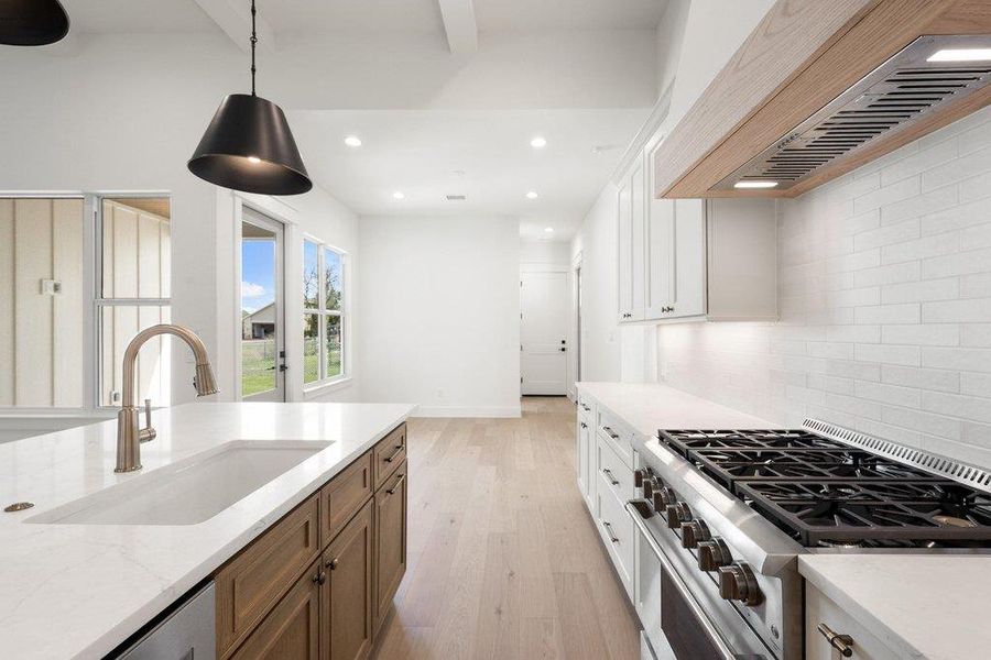 The kitchen features a large island with a sink and a modern faucet, white countertops, and a stainless steel range with a wooden hood