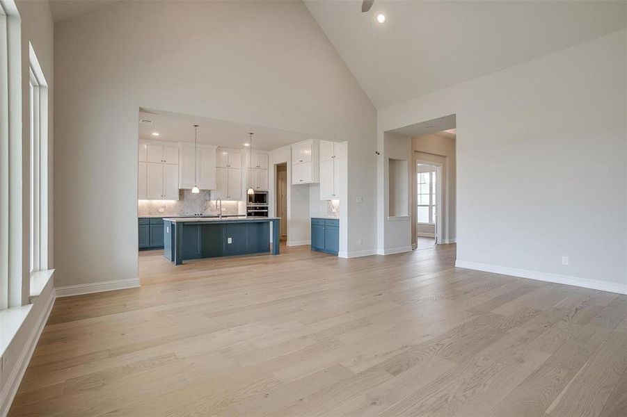 Unfurnished living room with light hardwood / wood-style floors, high vaulted ceiling, and sink