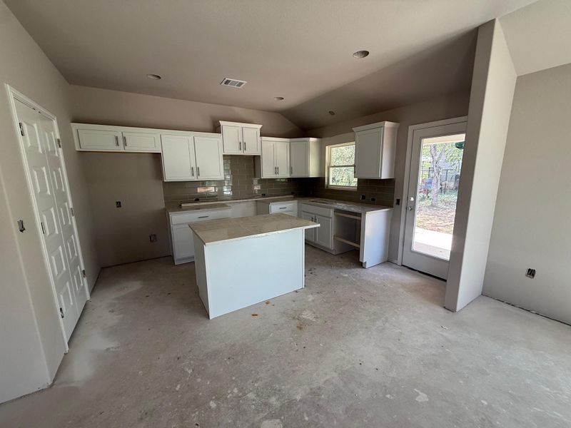 Kitchen with a kitchen island, decorative backsplash, unfinished concrete floors, vaulted ceiling, and white cabinetry