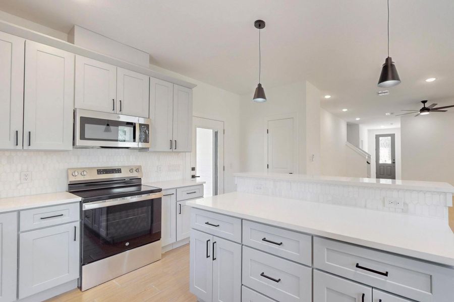 Kitchen with stainless steel appliances, pendant lighting, light wood finished floors, tasteful backsplash, and a ceiling fan