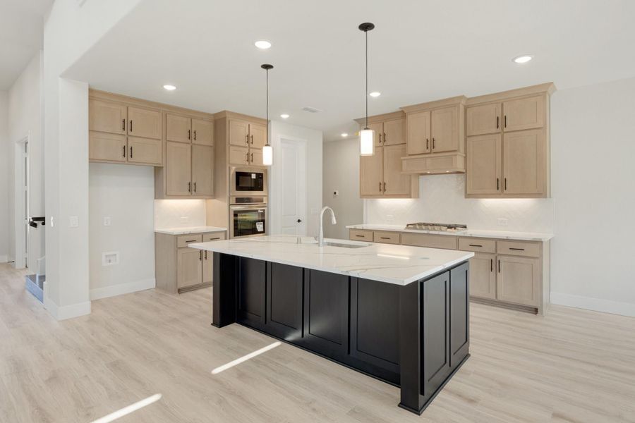 Kitchen with large black island, white quartz countertops, light wood cabinets, and pendant lights over light hardwood floors.