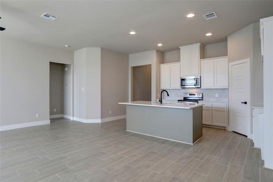 Kitchen with a kitchen island with sink, stainless steel appliances, tasteful backsplash, light hardwood / wood-style floors, and white cabinets