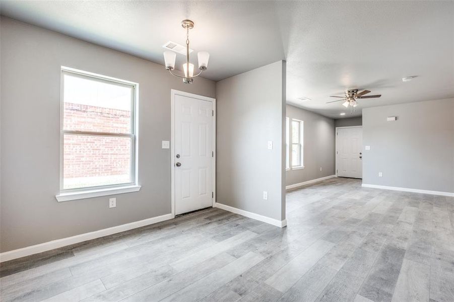 Spare room featuring ceiling fan with notable chandelier and light hardwood / wood-style floors