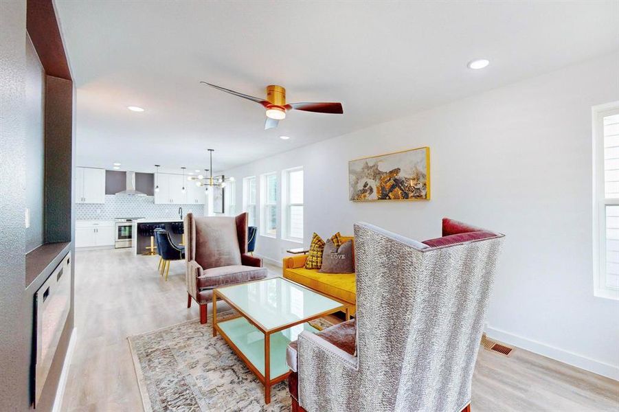 Living room featuring ceiling fan with notable chandelier and light hardwood / wood-style flooring