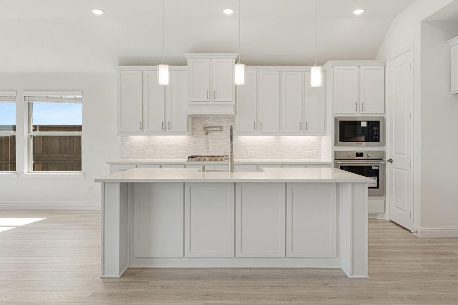White kitchen with large island, pendant lights, tile backsplash, and stainless steel built-in appliances White kitchen with large island, pendant lights, tile backsplash, and stainless steel built-in appliances
