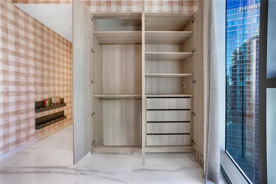 Built-in storage cabinet with wood-finish shelving and soft-close drawers, floor-to-ceiling windows, and large-format neutral-tone tile flooring