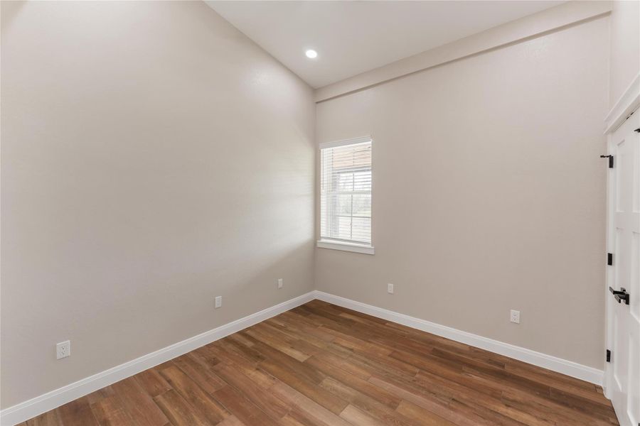 This room features neutral taupe walls, tile wood-style flooring, and a high ceiling with recessed lighting. A window provides natural light, and there's a white door with modern hardware.