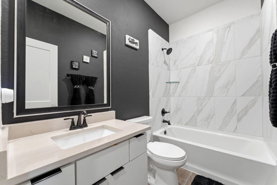 Modern full bathroom with quartz countertop vanity, designer fixtures, and tiled tub/shower combination.