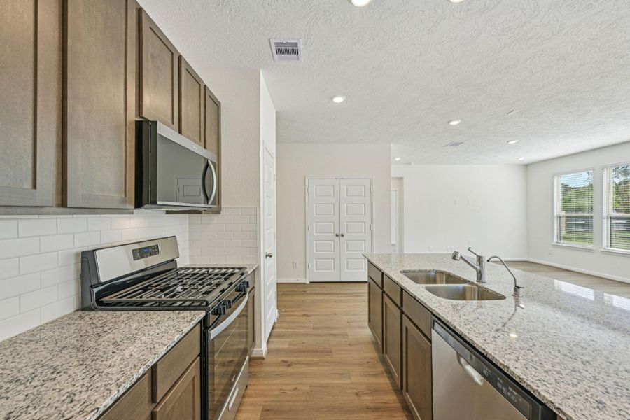 The kitchen features high ceilings, stained wood cabinets, granite countertops, SS appliances including microwave, modern tile backsplash, recessed lighting, and a pantry all overlooking your huge Great Room.