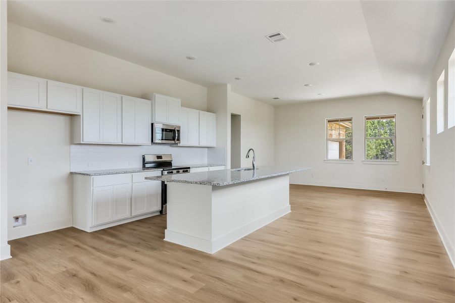 Kitchen featuring stainless steel appliances, white cabinetry, a kitchen island with sink, light wood-type flooring, and light stone counters