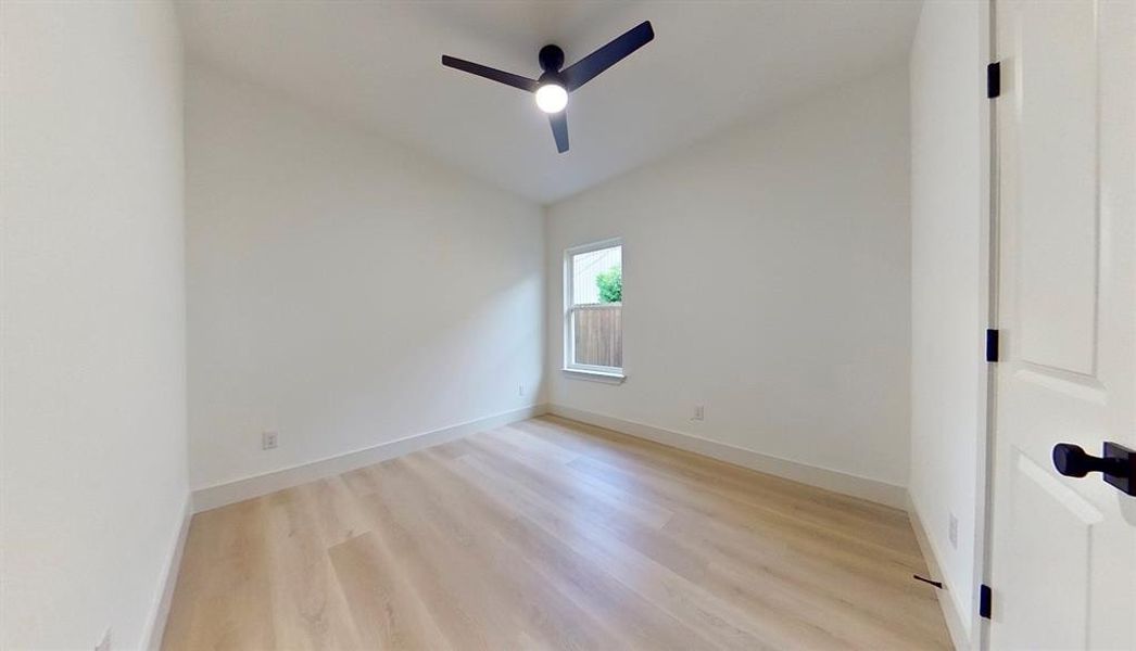 Bright interior room featuring wood-finish flooring, a contemporary ceiling fan, and a single window with a privacy fence visible beyond