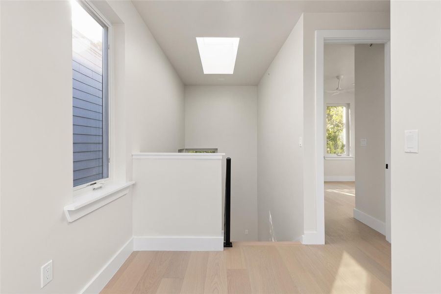 Natural light pours through a large skylight over the wood-floored landing and staircase area.