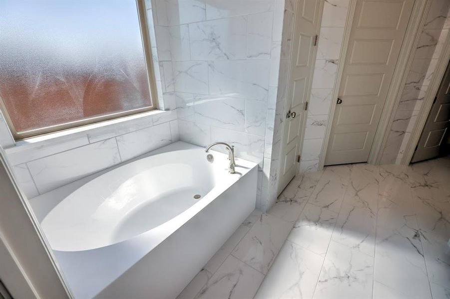 Full bathroom featuring light marble finish floors, a garden tub, and tile walls Full bathroom featuring light marble finish floors, a garden tub, and tile walls