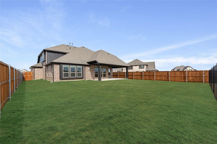 Backyard of brick home with large green lawn, covered patio, and wood privacy fence Backyard of brick home with large green lawn, covered patio, and wood privacy fence
