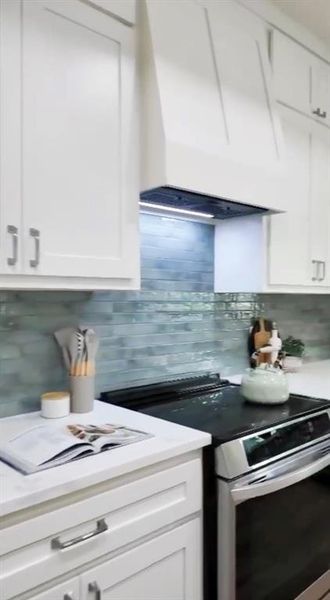 White shaker-style cabinetry with satin nickel hardware, a custom range hood, and a light blue tile backsplash