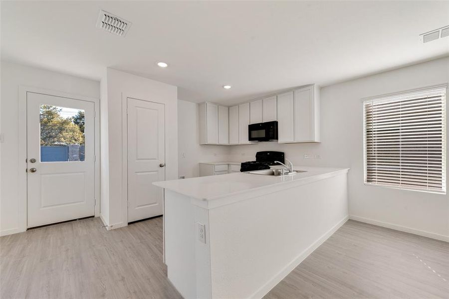 Kitchen with black appliances, sink, kitchen peninsula, light wood-type flooring, and white cabinetry