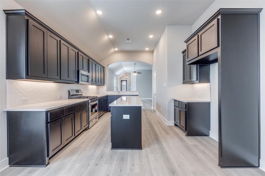 Kitchen featuring appliances with stainless steel finishes, ceiling fan, vaulted ceiling, backsplash, and a center island