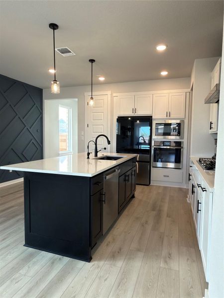 Kitchen featuring a large island with white countertop, black cabinetry, and an integrated stainless-steel dishwasher