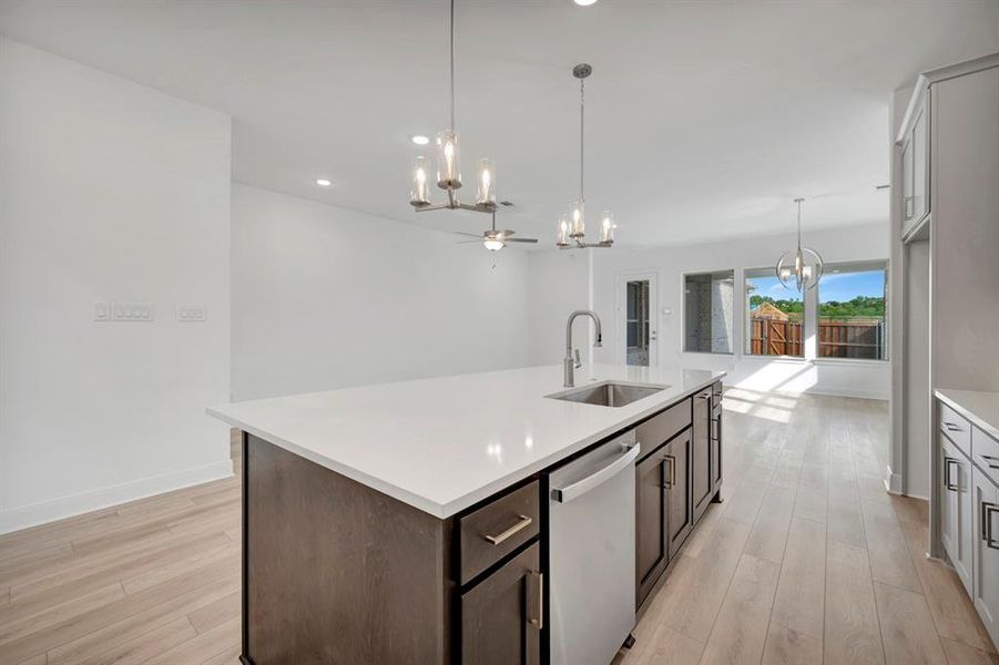 Kitchen with hanging lights, stainless steel dishwasher, light wood-style flooring, and a center island with sink Kitchen with hanging lights, stainless steel dishwasher, light wood-style flooring, and a center island with sink