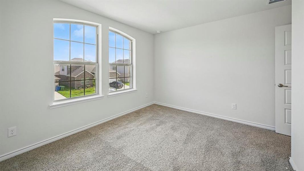Spacious room featuring two arched windows, light gray carpeting, crisp white walls, white baseboards, and a paneled interior door Spacious room featuring two arched windows, light gray carpeting, crisp white walls, white baseboards, and a paneled interior door