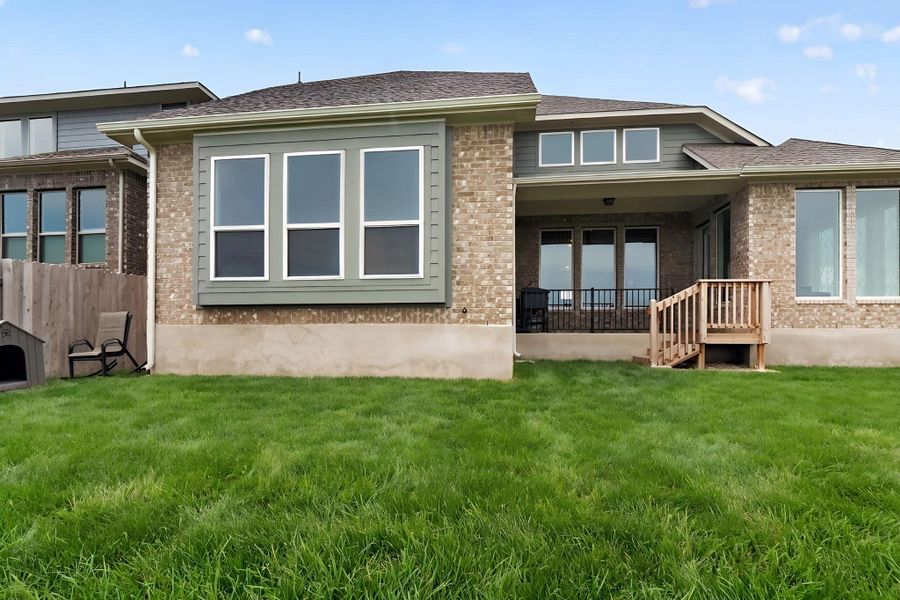 Rear exterior featuring a brick facade with a covered patio, wood deck, and a green lawn Rear exterior featuring a brick facade with a covered patio, wood deck, and a green lawn
